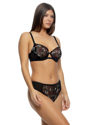 A woman standing at a side angle wearing an unlined embroidered bra in black with floral details and matching panties