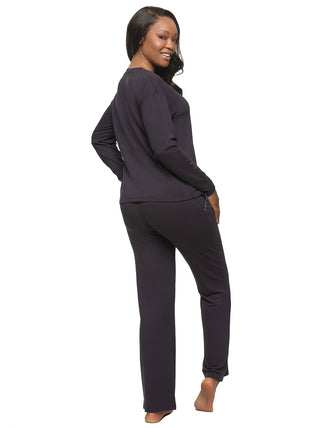 A woman wearing a navy bulue 2-piece lounge set with a long-sleeved pullover and pants, both with velvet trim, standing with hands in pockets. - back view