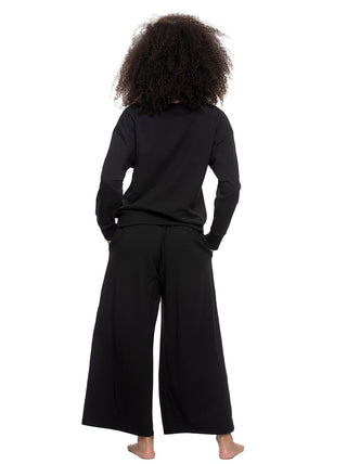 Woman wearing a black outfit - a sweatshirt with wide-leg pants on a white background