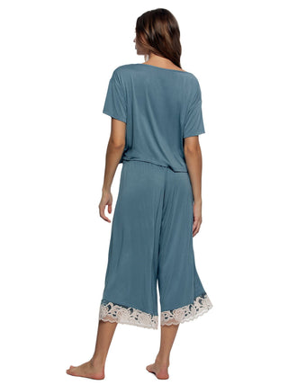 Woman wearing a teal pajama set  shirt and wide pants with lace trim on a white background back view
