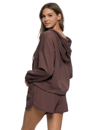 Woman wearing a brown hoodie and shorts set on a white background. back view
