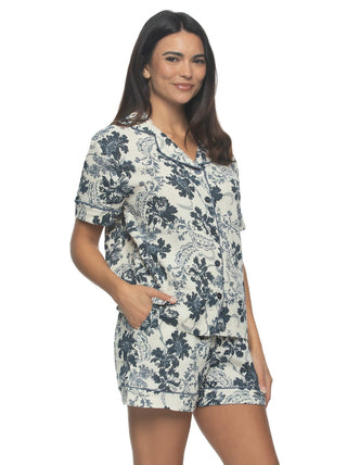 Kyra A woman wearing a white and blue floral pajama shorts set with a button-down shirt and drawstring shorts, model has hand in shorts pocket, standing against a plain background.