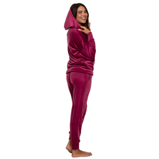 Woman wearing a burgundy velvet zip-up hoodie fwith hood on and matching pants on a white background back view